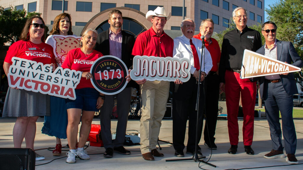 A group of people holding TAMU victoria signs and smiling