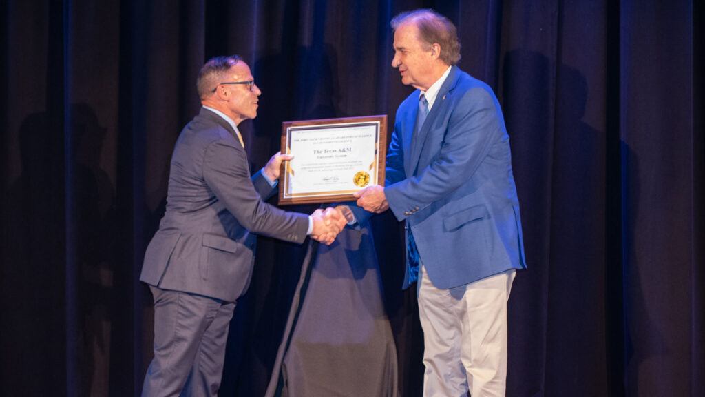 Chancellor John Sharp receives the award from Major General Daniel J. Lecce, USMC (Ret.), on stage.