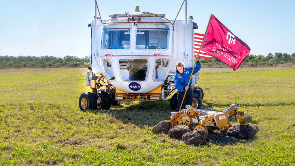 A woman plants a Texas A&M Space Institute flag in the ground with a NASA rover vehicle in the background