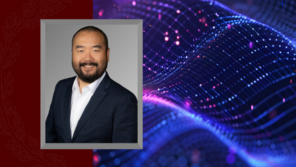 Headshot of a man in a suit against a graphic background featuring maroon accents and an abstract blue digital wave.